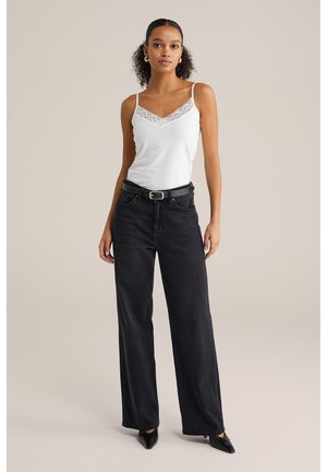 Hvid camisole med blonder, parret med højdenede sorte brede jeans og sorte hæle, med et sølvbælte og enkle accessories.