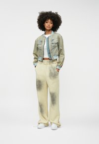 Svijetloplava traper jakna bomber sa dva prednja džepa, nosi se preko bijelog crop topa. Bež trenerke imaju tamnosive mrlje. Bijele tenisice.