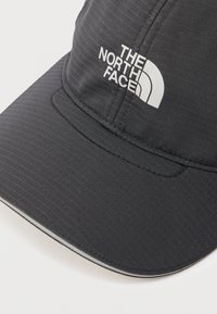 Black textured baseball cap with white "THE NORTH FACE" logo on the front panel, resting on a white surface.