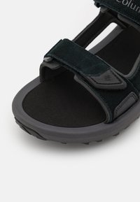 Sandalia negra de punta abierta con correas de ante, plantilla acolchada y suela de goma texturizada. Los cierres ajustables de velcro mejoran la comodidad.