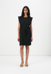 Black dress made of soft fabric, featuring ruffled sleeves and a drawstring waist. Flat sandals with crisscross straps complement the outfit.