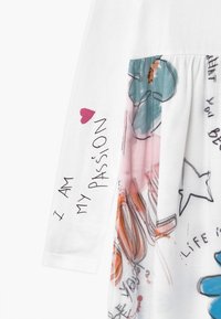 Biała sukienka z długimi rękawami, z kolorową drukowaną spódnicą z wzorami i tekstem. Tekst zawiera "JESTEM MOJĄ PASJĄ" oraz zabawne grafiki.