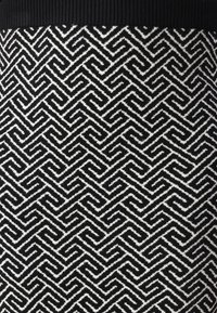 Tissu tricoté noir et blanc présentant un motif en zigzag, avec une surface texturée et une taille côtelée noire unie en haut.