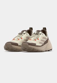 Αθλητικά παπούτσια σε ανοιχτό μπεζ με σκούρες καφέ λεπτομέρειες. Διαθέτουν υφή στη σόλα, κορδόνια με πορτοκαλί τονίσματα και θηλιά για ευκολία στο φόρεμα.