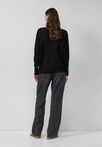 Zwarte geribbelde trui met verlaagde schouders, gecombineerd met high-waisted donkergrijze jeans en bruine schoenen. Eenvoudige en relaxte pasvorm.