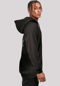 Black hoodie made of soft fabric, featuring a front kangaroo pocket, ribbed cuffs, and an intricate graphic design on the back.