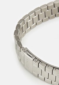 Hõbedane roostevabast terasest kella rihm, millel on ristkülikukujulised lingid, poleeritud ja matt viimistlus, varustatud kinniseguga, millel on graveeritud logo.