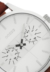 Silver stainless steel watch with a textured white dial, black sub-dials, and a brown leather strap. Features white hour markers and hands.