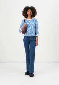 Blå och vit mönstrad topp med trekvartsärmar, i kombination med högmidjade mörkblå utsvängda jeans och svarta platåskor, samt en bourgognefärgad väska.