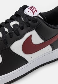 Basket en cuir noir avec des accents blancs et bordeaux, présentant un swoosh Nike bordeaux proéminent, une surface texturée et des lacets noirs.