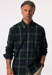 Camisa de cuadros de manga larga en verde oscuro y marino, con líneas blancas, cuello abotonado y mangas con puños. Tejido texturizado con un bolsillo frontal.
