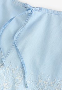 Světle modrá džínová látka s bílou květinovou výšivkou. Obsahuje zavazování. Hladká textura s neformálním designem.