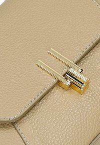 Beżowa skórzana torebka o teksturowanej powierzchni z metalowym zapięciem w złotym kolorze. Posiada przeszycia wzdłuż krawędzi oraz elegancki, prostokątny kształt.