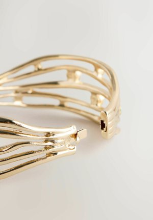 Gold-tone cuff bracelet with an organic, open design featuring elongated, curved lines and a clasp mechanism. Smooth finish with a shiny texture.