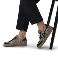Des baskets avec un design à imprimé léopard, des accents noirs, des lacets blancs et une semelle en gomme. Le matériau semble texturé, complétant des pantalons noirs décontractés.