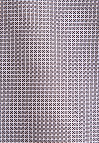 Herhalend geometrisch patroon op stof met kleine ronde vormen in donkerblauw en bruin op een lichte achtergrond. Textiel met een gladde textuur.