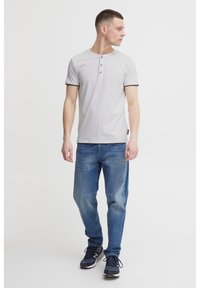 Light gray short-sleeve henley t-shirt with three-button placket, black trim on sleeves, paired with blue denim jeans and black sneakers.
