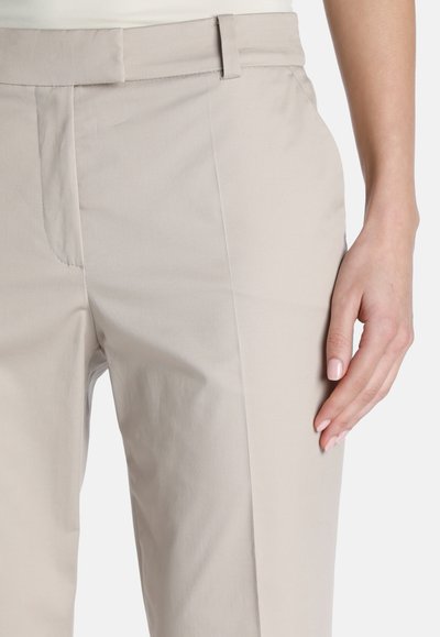 Beige housut, jotka on valmistettu kevyestä kankaasta, suoran leikkuun omaavat, sivutaskuilla varustetut ja sileä rakenne hienovaraisella ompeleella.