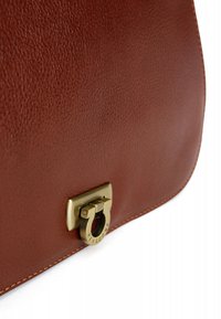 Sac à main en cuir marron avec une surface texturée, présentant un fermoir en laiton de design circulaire et un détail gravé "Hexagona".