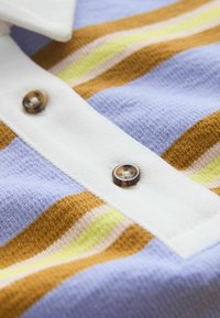 Gros plan d'un vêtement tricoté à rayures horizontales en moutarde, lavande, jaune et crème, avec une patte de boutonnage blanche ornée de boutons marron.