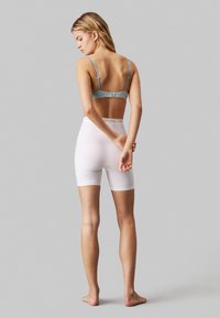 Bra regolabile di un blu chiaro e pantaloni corti bianchi a vita alta, caratterizzati da una texture liscia, una vestibilità aderente e una cintura elastica con marchio.