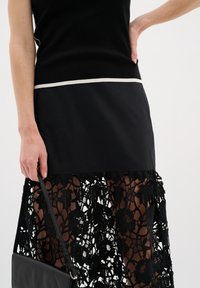 Black top with a cream horizontal stripe, paired with a black skirt featuring intricate lace and floral patterns, and a textured leather bag.