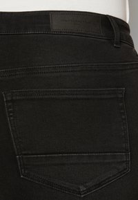 Črne jeans hlače iz denima z gladko teksturo, ki imajo zadnji žep in blagovno usnjeno nalepko na pasu, na kateri je napis "ONLY CARMAKOMA."