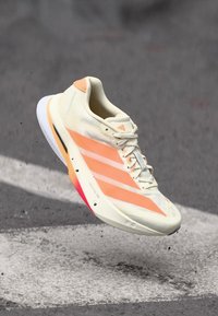 Baskets légères couleur crème avec des accents corail. Elles disposent d'une tige en maille respirante, de trois bandes blanches, et d'une semelle douce et rembourrée.