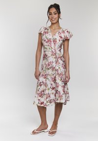 Robe à motif floral avec de courtes manches bouffantes, détail froncé sur le côté et ourlet évasé. Couleurs principalement rose et verte sur un fond clair.