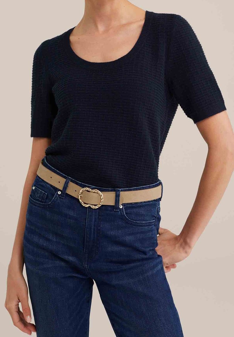 Toppik korte rukavi u mornarsko plavoj boji s teksturom uparen s tamnoplavim trapericama visokog struka i bež remenom s pozlaćenim zakovom u obliku uvijene vrpce.