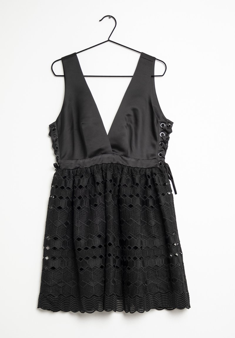 Robe noire avec un décolleté en V profond, corsage en satin, détail lacé sur les côtés et jupe à motif hexagonal texturé. Suspendue à un crochet noir.