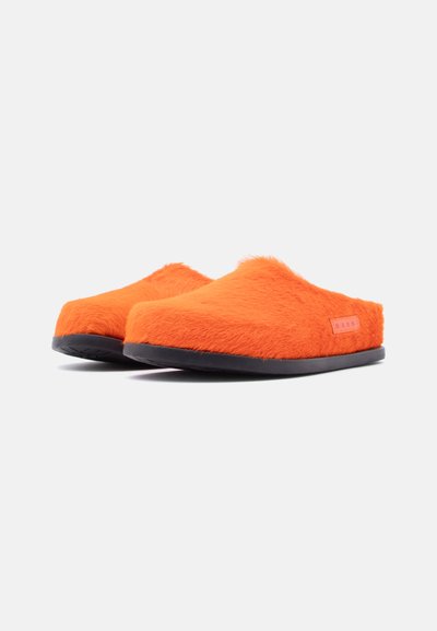 Chaussons orange pelucheux à enfiler avec une tige texturée et une semelle en caoutchouc noire. Présentent une petite étiquette rose sur le côté.