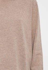 Jasnobrązowy sweter z dzianiny wykonany z miękkiego materiału, z okrągłym dekoltem, długimi rękawami oraz gładką fakturą z delikatnymi różnicami.