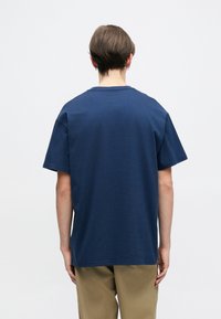 Mornarsko modra kratka majica s kratkimi rokavi iz mehke bombažne tkanine, s krožnim ovratnikom in sproščenim fitom z gladko teksturo. Opazna podrobnost šivanja.