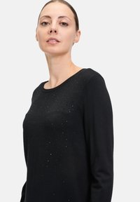 Maglione nero a maniche lunghe con scollo rotondo e decorazioni testurizzate, con piccoli dettagli scintillanti sulla parte anteriore.
