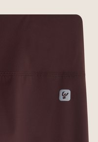 Leggings atletici bordeaux realizzati in tessuto liscio con cuciture piatte, dotati di un piccolo logo grigio sul lato sinistro in basso.