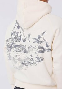 Crème hoodie met zwart vintage illustratie van een vrouw, vogels en wolken op de achterkant, voorzien van verhoogde witte parelaccenten.
