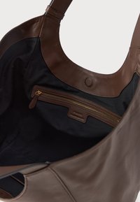 Bolsa tote de couro castanho com um exterior suave, apresentando um forro de tecido preto e um bolso interior com fecho zip e hardware dourado.