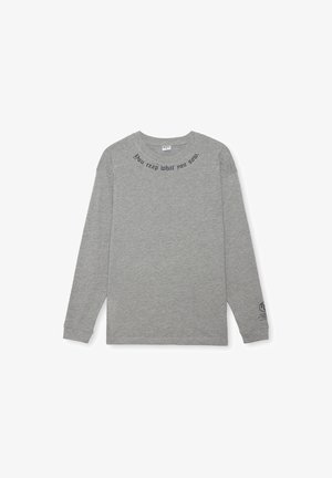 Camiseta de manga larga gris hecha de algodón, con cuello redondo y texto impreso en negro en la parte superior y cerca del puño izquierdo.