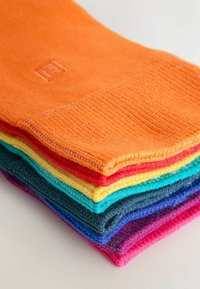 Kolorowe skarpetki ułożone w stos, prezentujące różnorodne żywe odcienie, w tym pomarańczowy, czerwony, żółty, morski, niebieski i fioletowy. Miękka tekstura.