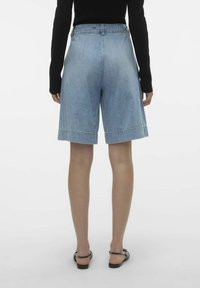 Shorts de mezclilla en azul claro, con un corte relajado, puños doblados y una cinturilla con pasadores para cinturón. Combinados con una blusa negra de manga larga.