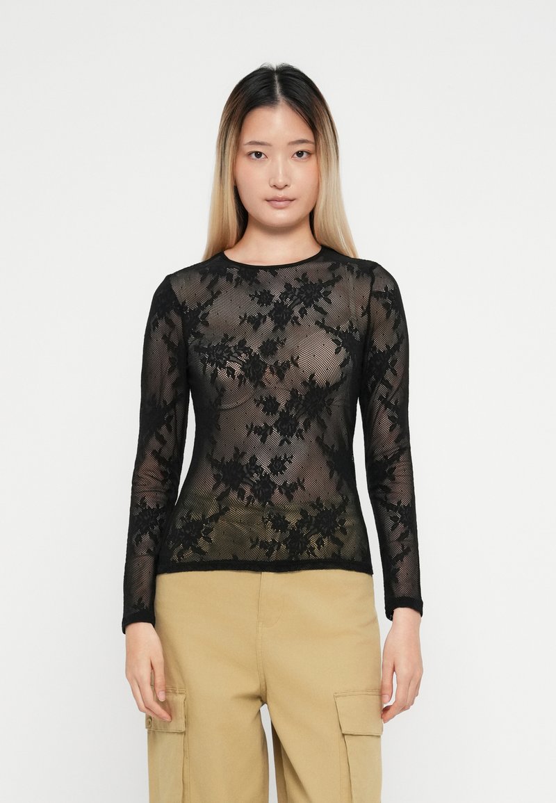 Top lungo a maniche nere in pizzo con motivi floreali, texture trasparente e scollatura rotonda; abbinato a pantaloni cargo beige.