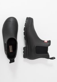 Black rubber ankle boots with textured outsole and elastic side panels. Features a pull tab at the back and a small logo label inside.