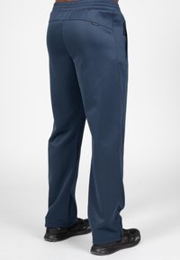 Navy sportbroek met een gladde textuur, elastische tailleband, zijzakken en taps toelopende benen, gecombineerd met zwarte sportschoenen.