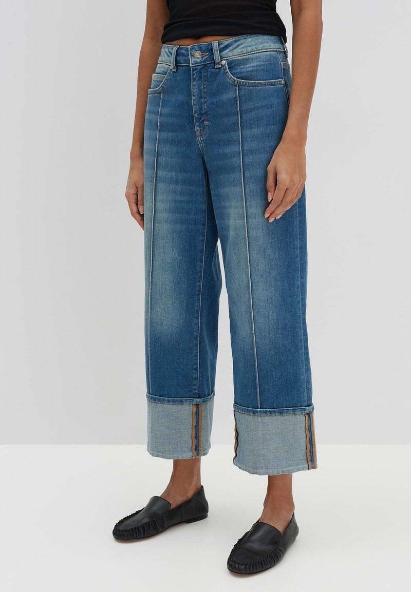 Jeans in denim a gamba larga con un lavaggio blu sbiadito, lunghezza cropped, con risvolti in denim a contrasto e dettagli delle cuciture in evidenza. Abbinati a scarpe nere senza lacci.