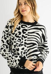 Schwarzer und weißer Strickpullover mit einem geteilten Design, das Leoparden- und Zebramuster zeigt, mit gerippten Bündchen und einem runden Ausschnitt.