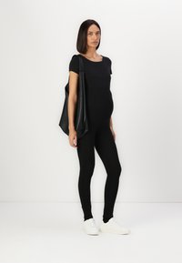 Črna majica s kratkimi rokavi, črne leggins hlače visoko pasu in bele športne teniske. Velika črna torba, obesena čez ramo. Gladek, elastičen material.