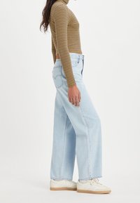 Ljusblå vida jeans i denim med hög midja, tillsammans med en långärmad topp i brunt och gult randigt mönster samt vita sneakers.