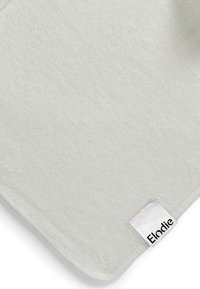 Pehmeä harmaa pyyhe, jossa on teksturoitu pinta, pyöristetty kulma ja valkoinen etiketti, jossa lukee "Elodie" mustalla.