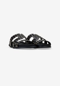 Sandalias negras con diseño recortado y tachuelas doradas, con correas anchas y suela plana, fabricadas con material sintético.